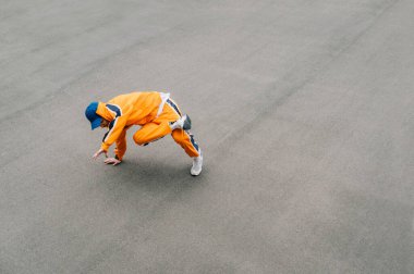 Turuncu eşofmanlı parlak bir dansçı kaldırımlı bir oyun alanında dans molası gösterisi sergiliyor. Profesyonel hip hop dansçısı sokaklarda dans ediyor. Geçmişi. Uzayı kopyala Üst görünüm.