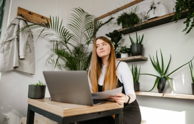 Hipster kafede dizüstü bilgisayarı ve elinde kağıtlarıyla oturan tatlı gülümseyen öğrenci kız, dalgın bir suratla başka yere bakıyor. Masadaki rahat kahve dükkanında dizüstü bilgisayarla çalışan serbest çalışan bir kız..