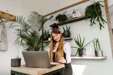 Gülümseyen serbest çalışan kız rahat bir laptopçu kafede bir masaya oturur ve olumlu bir surattan bilgi okur. Bayan öğrenci dersten önce kafede ders çalışıyor ve gülümsüyor..