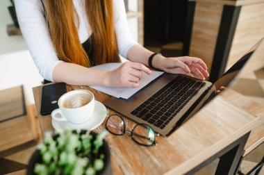 Yakın çekim fotoğrafı. Öğrenci kız elinde dizüstü bilgisayarla kafeteryada kahve içip ders çalışıyor. Bayan Freelancer laptopta çalışıyor ve bir kafede kahve içiyor. Bir kafede çalışıyor. Arkaplan