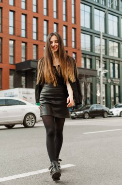 Yüzünde bir gülümsemeyle caddede yürüyen resmi giyinmiş çekici bir kadının uzun bir portresi. Genç ve güzel bir iş kadını şehirde dolaşıyor, kameraya bakıyor ve gülümsüyor.