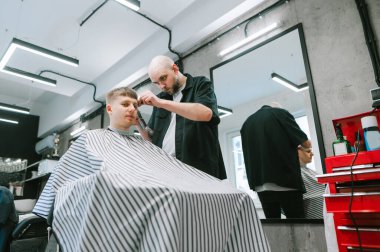 Berber dükkanında şık bir saç kesimi yaratma süreci. Hafif bir erkek kuaföründe çalışan bir atmosfer. Genç adam saçını bir berberde kesiyor ve kameraya bakıyor. Berber müşteriyi keser