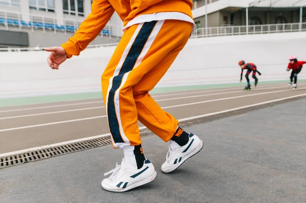 Hip hop dancer in bright clothes dancing on the stadium sports track,close up photo of legs.Legs of young man in orange pants dancing hip hop on sports track against roller skates.Background