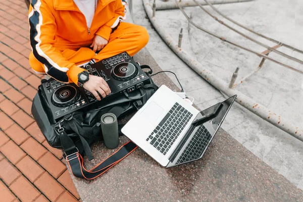 DJ plays music set on the street while walking, sits with an audio controller, laptop and speaker, close up photo. DJ man working outdoors with music mixer. Electronic music concept.
