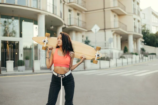 スタイリッシュな女の子のスケートボードは 深刻な顔で離れて見て 彼女の手の中に長いボードで通りに立っています ウォーキング中のスケートボードを持つパニックの女の子の肖像画 スペースのコピー — ストック写真