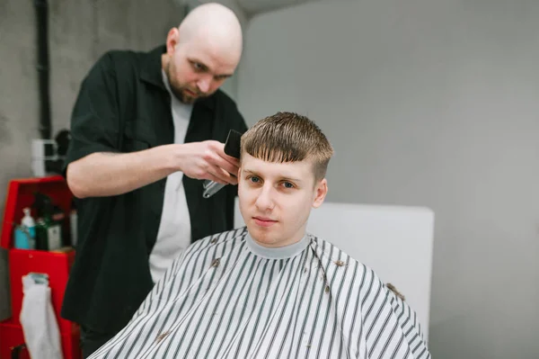 Joven Guapo Sienta Silla Barbero Corta Pelo Peluquero Mira Cámara — Foto de Stock