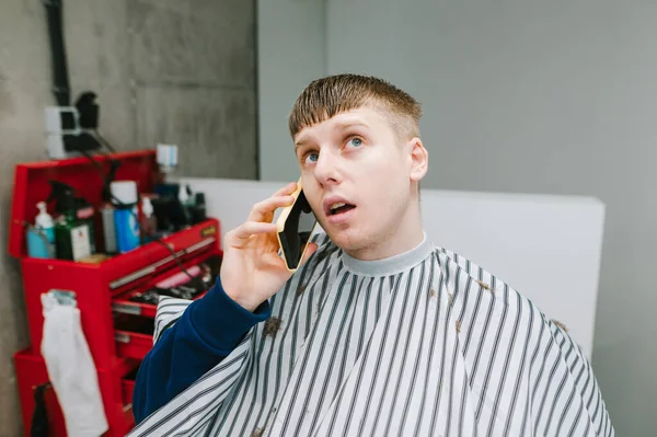 Portrett Overrasket Ung Mann Iført Frisør Sittende Frisørstol Snakke Telefonen – stockfoto