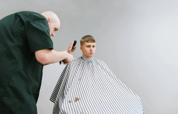 Barbiere Tagliare Capelli Del Giovane Uno Sfondo Grigio Cliente Guardando — Foto Stock