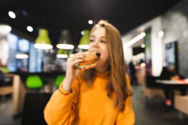 Bulanık. Soyut. Geçmişi. Fast food restoranında lezzetli burger yiyen mutlu kız. Masada bir kafede hamburger yiyen bir kadın. Boşluğu kopyala