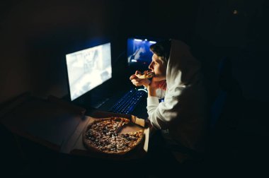 Oyuncu geceleri bilgisayar başında oturur, bilgisayarı kullanır ve kutudan pizza yer. Geceleri bilgisayarda çalışan ve pizza yiyen genç bir adamın portresi. Fast food ve gece işi..