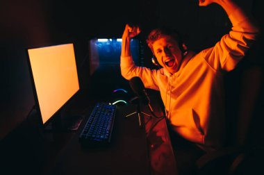 Kulaklıklı neşeli oyuncu video oyunu kazanıyor, kameraya bakıyor ve gülümsüyor. Mutlu adam flamalı bilgisayar oyunu oynar ve mikrofona konuşur, kameraya bakar ve sevinir..