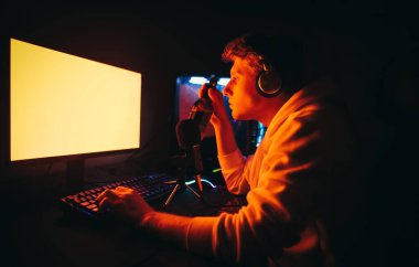 Kulaklık takan ve evde video oyunu oynayan genç bir adamın portresi, kırmızı ekrana bakıyor ve elinde bira şişesi tutuyor. Oyuncu bilgisayar oyunları oynuyor ve bira içiyor.