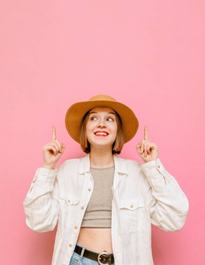 Açık yaz elbiseli güzel bir bayan sarı arka planda duruyor, başparmaklarını kaldırıyor ve fotokopi odasına bakıyor, şapka, bluz ve tişört giyiyor. Boş alana parmaklarını gösteren mutlu bir turist kızı.