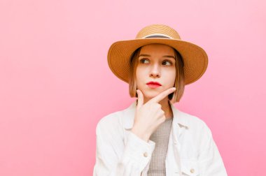 Yazlık kıyafetleri ve şapkası olan düşünceli çekici bir kız fotokopi odasına bakıyor ve düşünüyor. Pastel pembe arka planda izole edilmiş düşünceli yüzlü bayan turist. Boşluğu kopyala