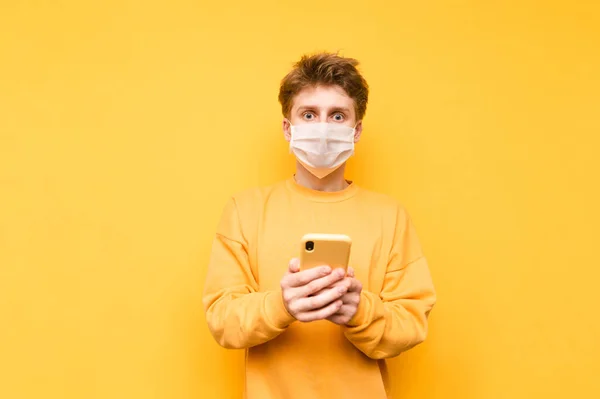 Shocked Young Man Protective White Mask Isolated Yellow Background Smartphone — Stock Photo, Image