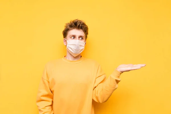 Surprised Guy Medical Mask Holds Copy Space His Hand Looks — Stock Photo, Image