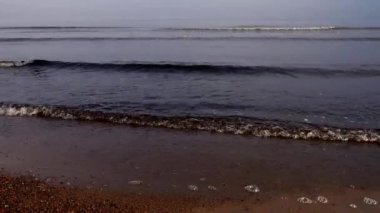 Waves rush to the sandy shore. Misty early morning.