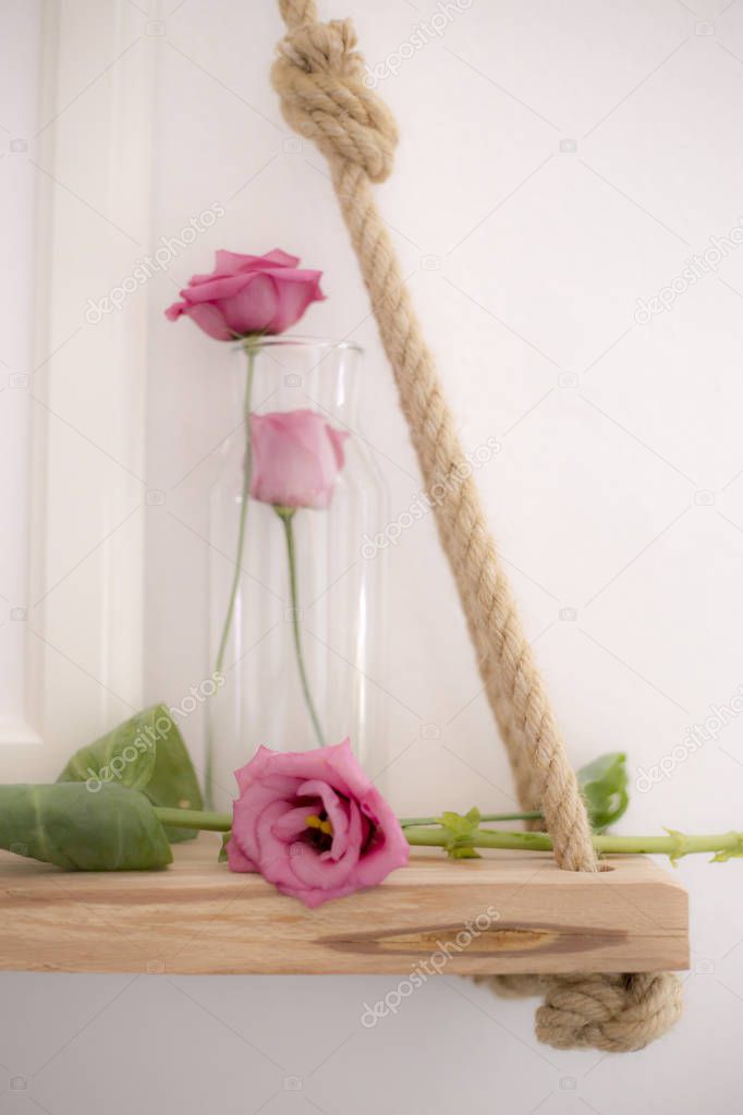 Closeup of pink roses and glass vase on hanged wooden shelf