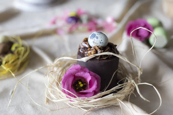 Closeup of mini chocolate cake for Easter. Holiday table decoration with Easter mini cake,  flower and colorful egg