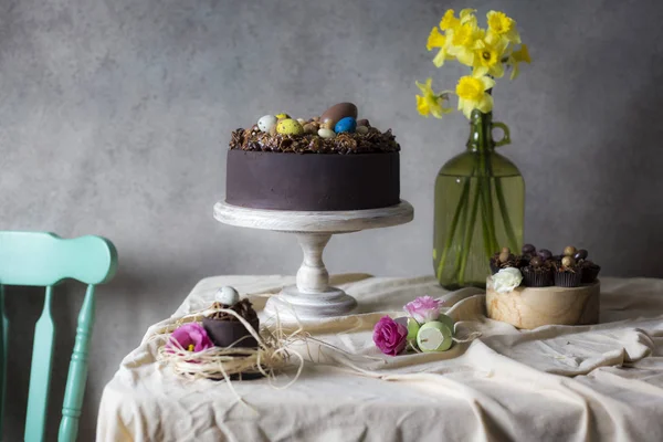 Chocolate cakes for Easter with flowers in vase. Holiday table decoration with Easter cakes,  flowers and colorful eggs