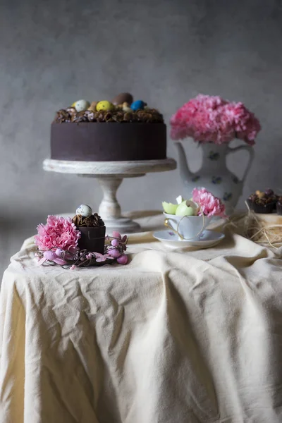 Chocolate cakes for Easter with flowers in vase. Holiday table decoration with Easter cakes,  flowers and colorful eggs