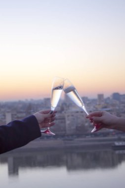 Closeup of female hands holding glasses of champagne on blurred city background. Women celebrating concept clipart