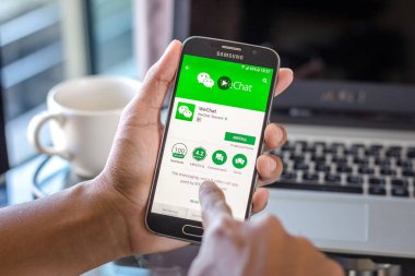 Chiang Mai, Tayland - 1 Şubat 2017: Asya adam Resepsiyon ofis üstünde belgili tanımlık perde üzerinde wechat uygulaması ile Samsung Galaxy S6 tutarak. İş çalışma alanı'nın Üstten Görünüm.
