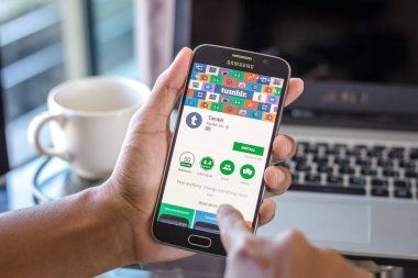 Chiang Mai, Tayland - 1 Şubat 2017: Asya adam tumblr app üstünde belgili tanımlık perde Resepsiyon Office ile Samsung Galaxy S6 tutarak. İş çalışma alanı'nın Üstten Görünüm.
