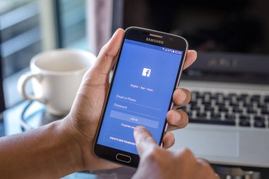 Chiang Mai, Tayland - 1 Şubat 2017: Asya adam facebook app üstünde belgili tanımlık perde Resepsiyon Office ile Samsung Galaxy S6 tutarak. İş çalışma alanı'nın Üstten Görünüm.