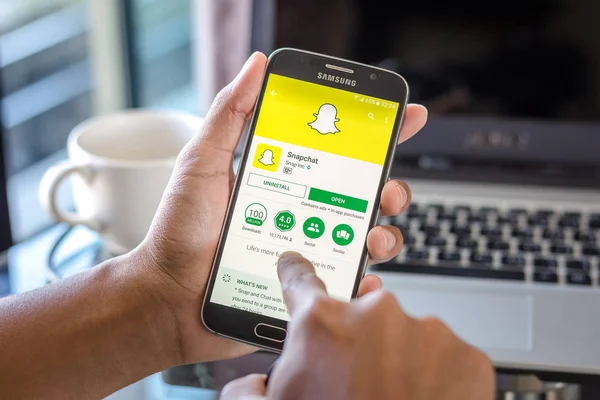 Chiang Mai, Tayland - 1 Şubat 2017: Asya adam Resepsiyon ofis üstünde belgili tanımlık perde üzerinde snapchat uygulaması ile Samsung Galaxy S6 tutarak. İş çalışma alanı'nın Üstten Görünüm.