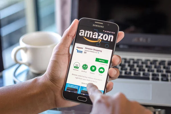 Chiang Mai, Tayland - 1 Şubat 2017: Asya adam üstünde belgili tanımlık perde üstünde Resepsiyon yazıhane app alışveriş amazon ile Samsung Galaxy S6 tutarak. İş çalışma alanı'nın Üstten Görünüm.