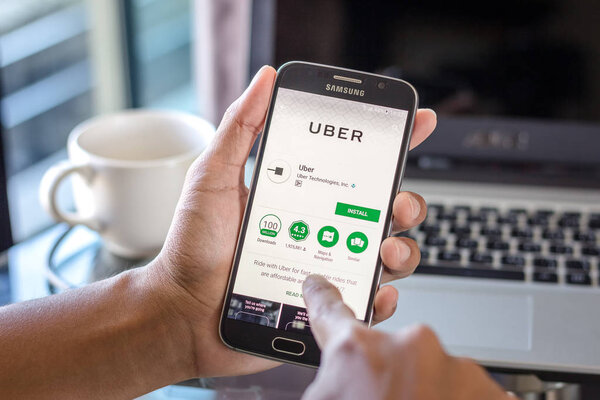 Chiang Mai,Thailand - February 1, 2017 : Asian man holding Samsung Galaxy S6 with uber taxi driver app on the screen on desk office. Top view of business workplace.