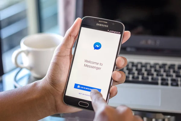 Chiang Mai, Tayland - 1 Şubat 2017: Asya adam facebook messenger app üstünde belgili tanımlık perde Resepsiyon Office ile Samsung Galaxy S6 tutarak. İş çalışma alanı'nın Üstten Görünüm.