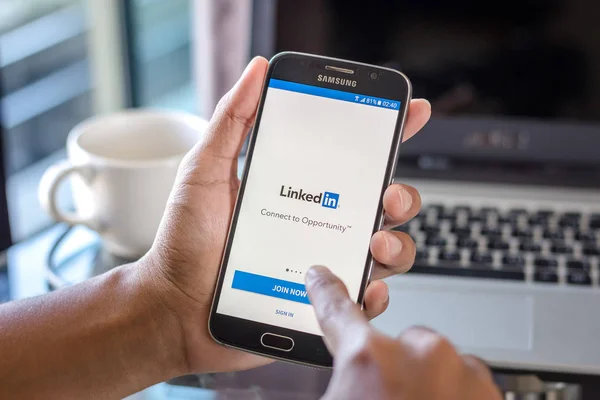 Chiang Mai, Tayland - 1 Şubat 2017: Asya adam LinkedIn app üstünde belgili tanımlık perde Resepsiyon Office ile Samsung Galaxy S6 tutarak. İş çalışma alanı'nın Üstten Görünüm.