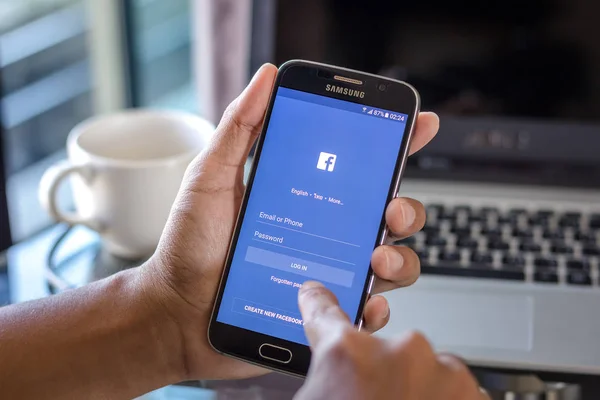 Chiang Mai, Tayland - 1 Şubat 2017: Asya adam facebook app üstünde belgili tanımlık perde Resepsiyon Office ile Samsung Galaxy S6 tutarak. İş çalışma alanı'nın Üstten Görünüm.