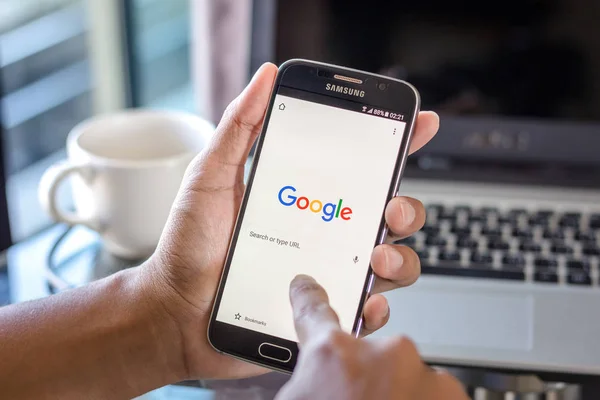 Chiang Mai, Tayland - 1 Şubat 2017: Asya adam Resepsiyon ofis üstünde belgili tanımlık perde üzerinde google arama uygulaması ile Samsung Galaxy S6 tutarak. İş çalışma alanı'nın Üstten Görünüm.