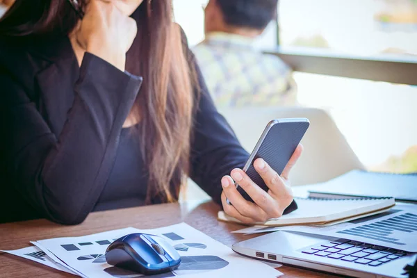 Bir smartphone ve bir dizüstü bilgisayar ile bir belgeyle bir kahve dükkanında çalışan kadar yakın işadamları.