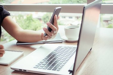 Bir smartphone ve bir dizüstü bilgisayar ile bir belgeyle bir kahve dükkanında çalışan kadar yakın işadamları.