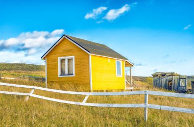 Terk edilmiş sarı küçük bir ev, kırsal kesimde beyaz çitli.