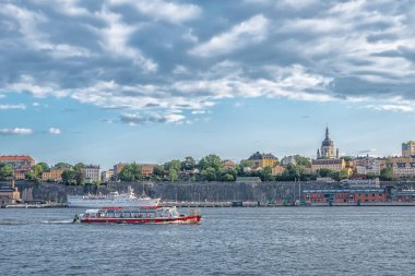 Wiev, Sodermalm adasının sahil şeridinde, turistik kırmızı teknesiyle.