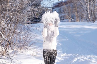 Güneşli kış gününde havaya kar atan genç bir kadın, o mutlu ve eğlenceli.