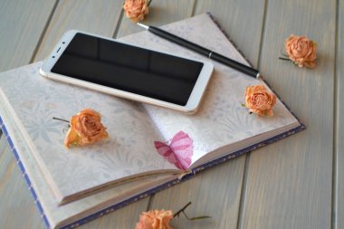 Kadınların yaşam tarzı için iş stili, eğitim veya motivasyon imajı. Not defteri, akıllı telefon ve klasik kuru güller.