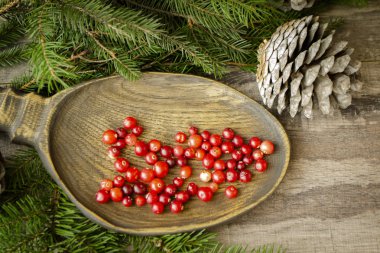 Ahşap bir masada yabani kırmızı kızılcıklar, yeşil dallı parlak bir görüntü, üst manzara.