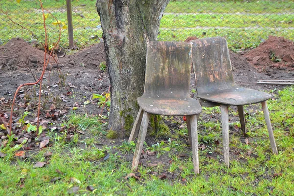 Dos viejas sillas de madera a la sombra de un árbol en el jardín de otoño. Imagen del problema social — Foto de Stock