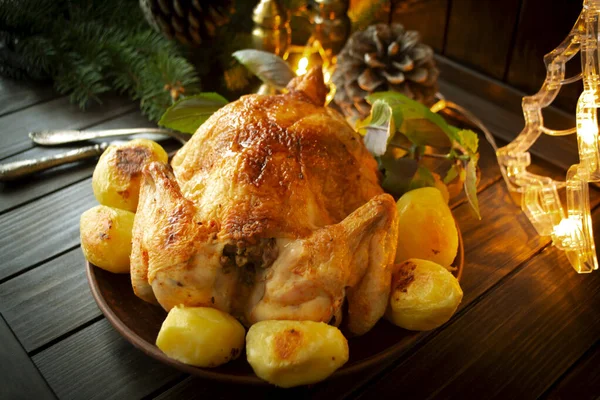 Roasted golden chicken with potatoes on rustic wooden table with Christmas decoration