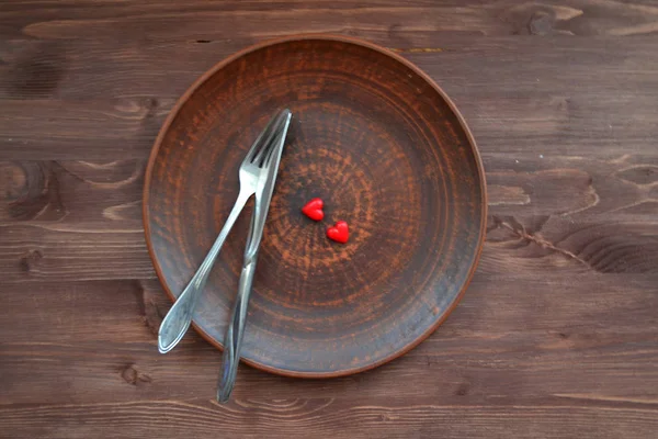 Empty ceramic plate with small red hearts on a dark wooden table — Stock Photo, Image