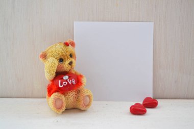 Elinde beyaz kartla oturan gülümseyen ayıcık. Mesaj atmak için boş bir yer, güzel bir alıntı ya da iyi bir ruh hali için sözler. Ön görünüm.