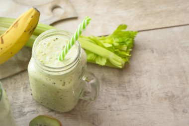 Kereviz, ıspanak, kivi, ahşap bir masada cam bir kavanozda muzdan yapılmış sağlıklı yeşil smoothie.