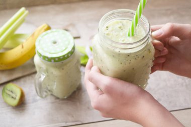 Yeşil sebze püresi, sağlıklı beslenme konsepti. Yeşil sebzeli detoks smoothie 'yi kereviz, muz, kivi ve ıspanakla kapat. Kadın elinde sebze kokteyli tutuyor.