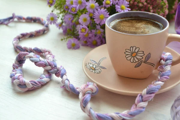 cup of coffee and flower on wooden background, image in violet, purple and white colors style life